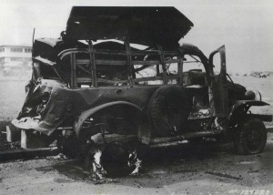 Heavily damaged truck at Hickam Field parked next to parade grounds with big barracks in background, December 7, 1941.