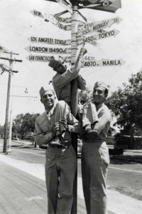 Soldier stands in front of Cross Roads of Pacific sign at Kau Kau Korner restaurant, Honolulu, 1940s. 