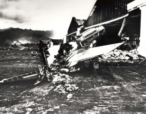 Severely damaged fighter plan sits in the midst of rubble in front of a burned out hangar at Wheeler Field, December 7, 1941.   