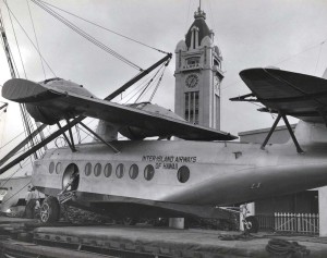 Inter-Island Airways. A Sikorsky S-43 is unloaded at Honolulu Harbor. Aloha Tower is in the background.