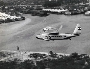Inter-Island Airways. Sixteen person U.S. air mail plane flying across industrial section of Honolulu Harbor at end of its daily 500-mile flight to various islands.