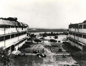 Looking out toward Hangar Avenue and the flight line from the courtyard between heavily damaged Wing E and Wing D of the big barracks at Hickam Field, December 7, 1941.   