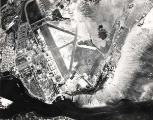 Hickam Field from 22,500 feet. Drainage canal from apex of runway and alluvial fan drainage at lower center. New railroad tracks at lower right, with old track still visible. Post exchange, clinic, officer's club, additional NCO and officer's quarters, warehouses, and engine shops, September 21, 1941. 