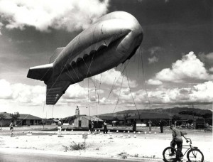Barrage balloon crew at Fort Kamehameha in World War II. The balloon ascends slowly while the passersby watch with interest. 