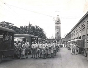 The first detachment of WACs to be in the Pacific Theater are loaded into buses at Aloha Tower for transfer to housing units, 1940s.   