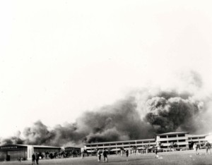 The first bombs to strike Hickam Field were dropped on parked planes and the hangar line, December 7, 1941. Personnel cross parade grounds in foreground to view damage. 