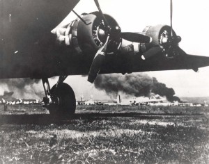 B-17 frames the devastating results from Japanese attack on Hickam Field, December 7, 1941. The smoke in the background is from USS Arizona which Japanese bombed. The B-17s arrived at Hickam the morning of the attack.