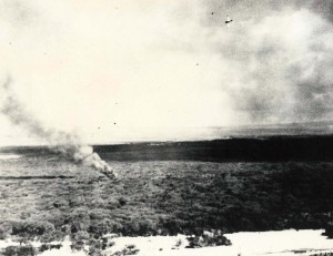 A downed Navy Scout Bomber Douglas (SBD) burns in Ewa as Japanese planes fly overhead, December 7, 1941.