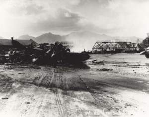Wrecked planes on Wheeler Field flight line with Hangar 2 in background and tent quarters where many enlisted men were killed, December 7, 1941.